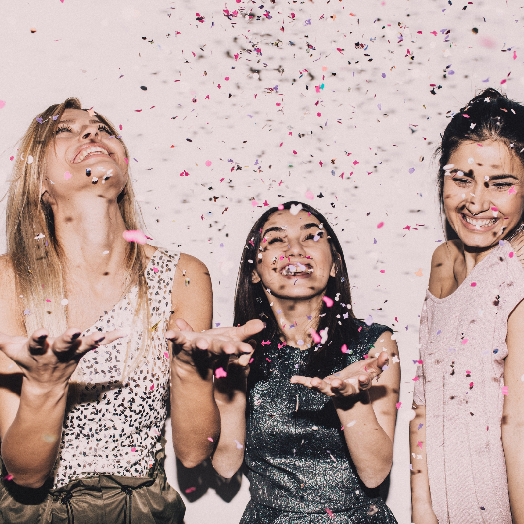 Three ladies catching confetti which is falling around them